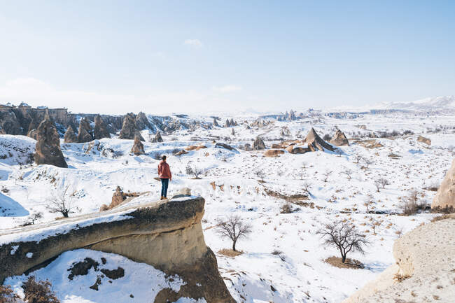 Von oben mit vollem Körper unkenntlich Mann Tourist auf Stein stehend und bewundern erstaunliche verschneite Landschaft Ansichten auf wolkenlosem blauem Himmel über schneebedecktem bergigem Gelände an sonnigen Wintertag in Kappadokien, Türkei — Stockfoto