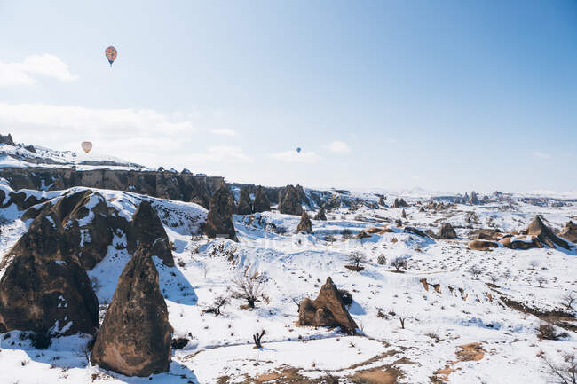 Vista incrível drone de balões coloridos de ar quente voando sobre o antigo assentamento Uchisar e terreno rochoso nevado com espectadores no dia frio de inverno na Capadócia, Turquia — Fotografia de Stock