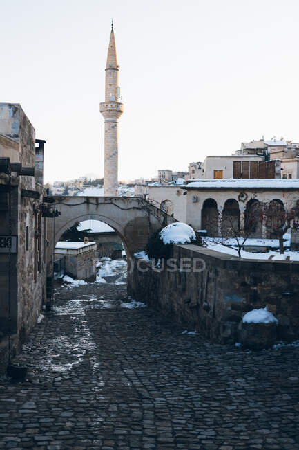 Leere Straße mit Pflastersteinen, die im Winter in der Türkei zwischen antiken Gebäuden zu einem hohen Minarettturm vor blauem Himmel führt — Stockfoto