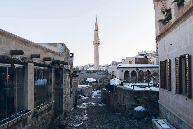 Leere Straße mit Pflastersteinen, die im Winter in der Türkei zwischen antiken Gebäuden zu einem hohen Minarettturm vor blauem Himmel führt — Stockfoto