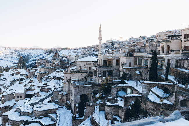From above small town with ancient buildings in valley and tall minaret tower on snowy hillside against cloudless blue sky in winter in Turkey — Stock Photo