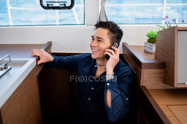 D'en haut du mâle souriant debout dans la cabine du yacht moderne et parlant sur téléphone portable — Photo de stock