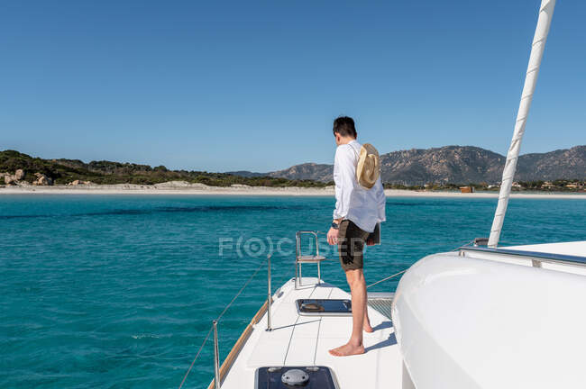 Back view of unrecognizable male in summer outfit standing on deck of  modern catamaran sailing in sea during summer vacation — blue sky, trip -  Stock Photo | #511663884