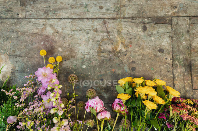 Вид сверху на различные свежие цветные цветы, расставленные рядами на старом столе в цветочном магазине — стоковое фото