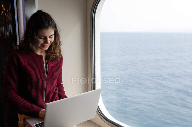 Contenu freelance femme voyageant sur un bateau de croisière et tapant sur ordinateur portable tout en travaillant sur le projet à distance en Sardaigne — Photo de stock