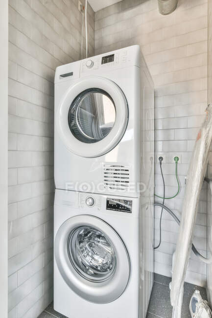 Interior de um espaço com máquina de lavar e secar roupa em uma casa ao lado de uma tábua de engomar e seu ferro — Fotografia de Stock