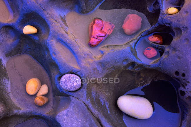 Desde arriba de fondo texturizado de guijarros coloridos surtidos colocados en roca en el agua - foto de stock