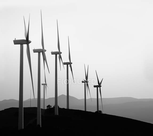 Mulini a vento contemporanei in bianco e nero disposti in fila su collina sullo sfondo della catena montuosa — Foto stock