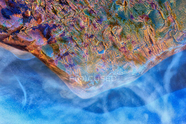 Abstract textured background of iridescent wet rock located near bright blue clean water — Stock Photo