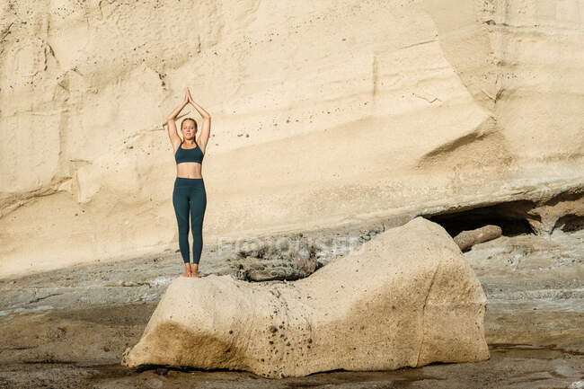 Young mindful female in sportswear on Tadasana pose with closed eyes while practicing yoga standing on rocky background — Stock Photo