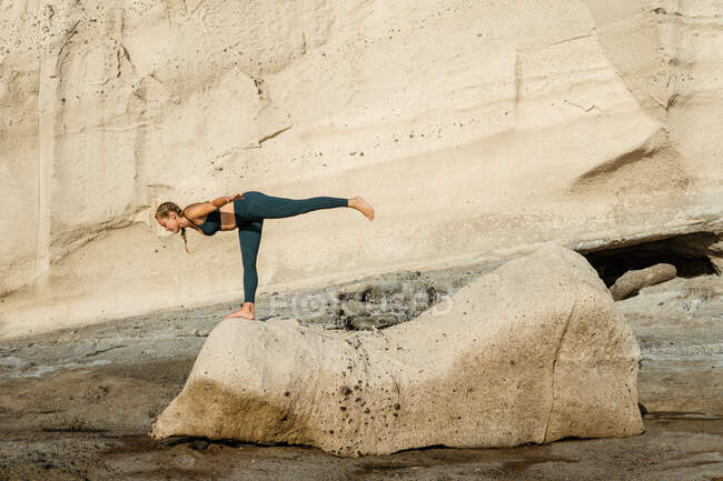Vista laterale della giovane donna in piedi con gamba sollevata mentre si appoggia in avanti durante la pratica dello yoga contro il monte — Foto stock