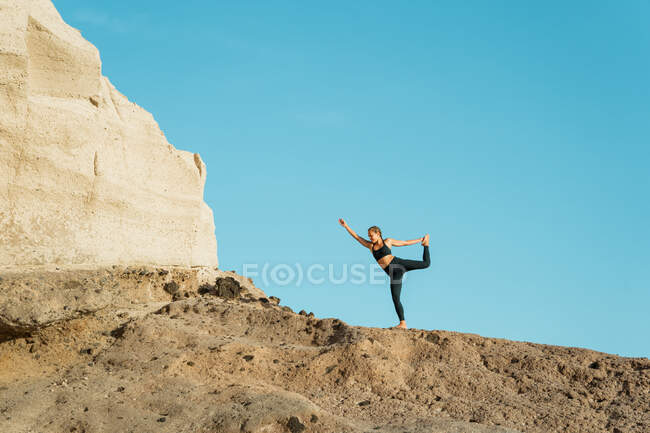 Junge Frau in Sportkleidung steht in Natarajasana-Pose, während sie tagsüber Yoga gegen den Berg praktiziert — Stockfoto