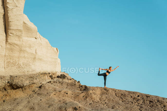 Junge Frau in Sportkleidung steht in Natarajasana-Pose, während sie tagsüber Yoga gegen den Berg praktiziert — Stockfoto