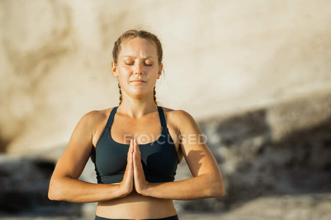 Giovane donna consapevole in abbigliamento sportivo meditando con gli occhi chiusi durante la pratica dello yoga su sfondo sfocato — Foto stock