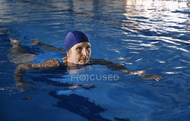 Орієнтована жінка середнього віку в купальнику плаває в басейні під час тренування з водної аеробіки — стокове фото