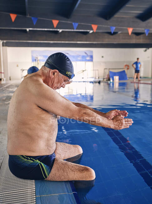 Вид збоку літнього чоловіка сидить біля басейну і розтягує руки під час тренувань з водної аеробіки — стокове фото