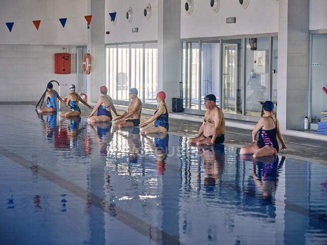 Группа людей в купальниках, сидящих у бассейна и растягивающих руки во время занятий водной аэробикой — стоковое фото