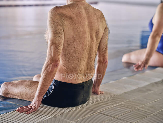 Вид ззаду анонімний літній чоловік сидить біля басейну і виконує вправи під час водної аеробіки — стокове фото