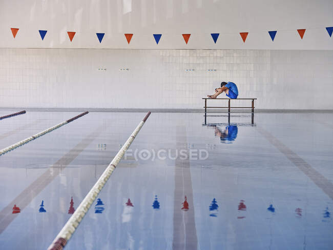 Вид сбоку тренера, растягивающего тело и обнимающего колени во время занятий водной аэробикой в бассейне — стоковое фото