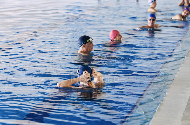Grupo de pessoas em bonés de natação em pé na piscina durante a aula de aeróbica aquática — Fotografia de Stock