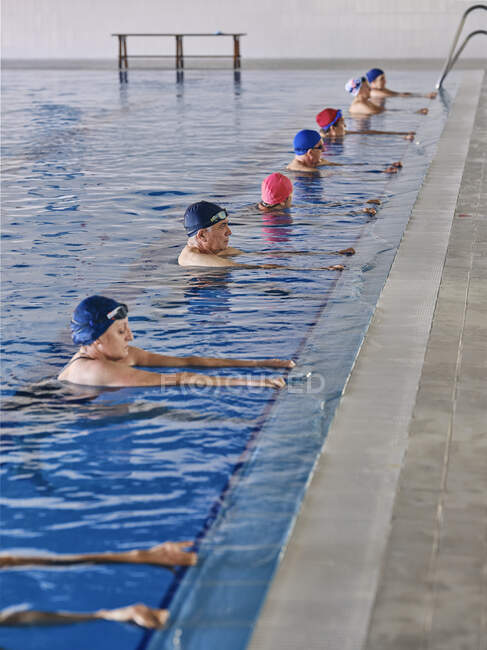 Группа людей в плавательных шапках, стоящих в бассейне во время занятий водной аэробикой — стоковое фото