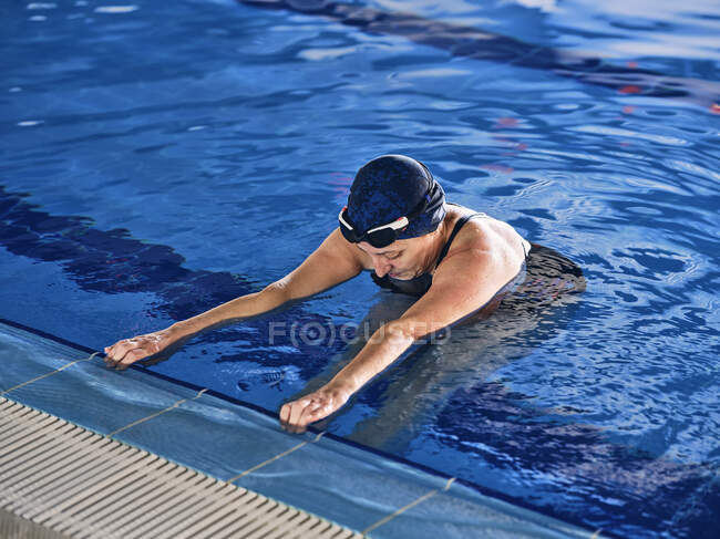 Зрелая женщина в плавательной шапочке, стоящая в бассейне во время занятий водной аэробикой — стоковое фото