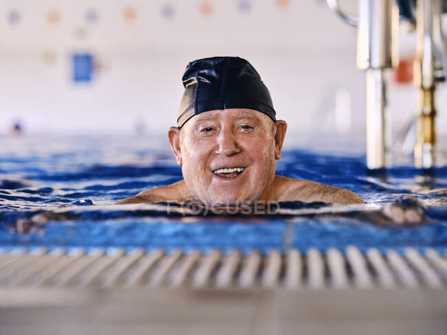 Восхитительный мужчина средних лет в кепке плавает в бассейне и делает упражнения во время занятий водной аэробикой — стоковое фото