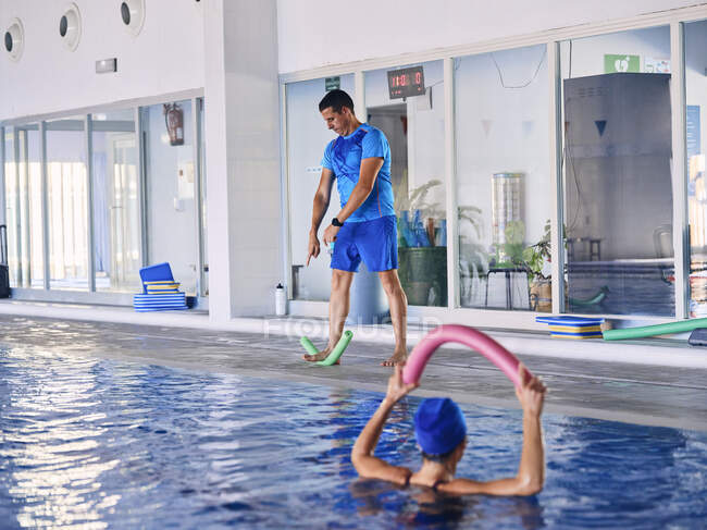 Feminino nadador exercitando com macarrão de espuma durante o treinamento de aeróbica aquática com treinador na piscina — Fotografia de Stock