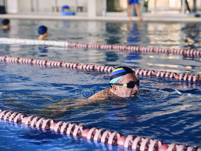 Чоловік середнього віку в окулярах і кепці плаває в басейні під час водної аеробіки — стокове фото