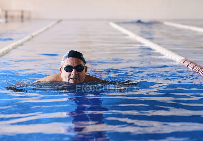Homme d'âge moyen dans des lunettes et bonnet de natation dans la piscine pendant l'aérobic aquatique — Photo de stock