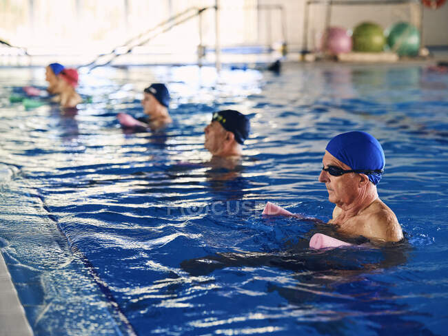 Seitenansicht einer Gruppe von Menschen in Badebekleidung, die während der Wassergymnastik mit Schaumwassernudeln im Pool üben — Stockfoto