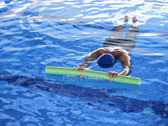 Сверху анонимная женщина плавает с пенной лапшой в бассейне во время занятий водной аэробикой — стоковое фото