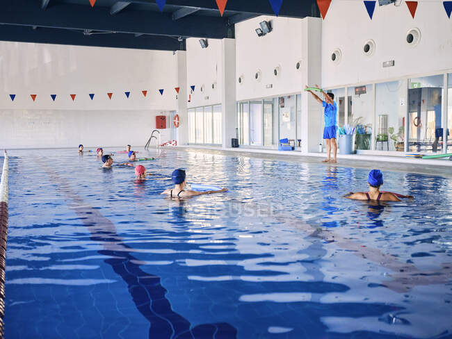 Група людей у плавальному спорті з локшиною аква в басейні з інструктором під час тренування з гідробіології. — стокове фото