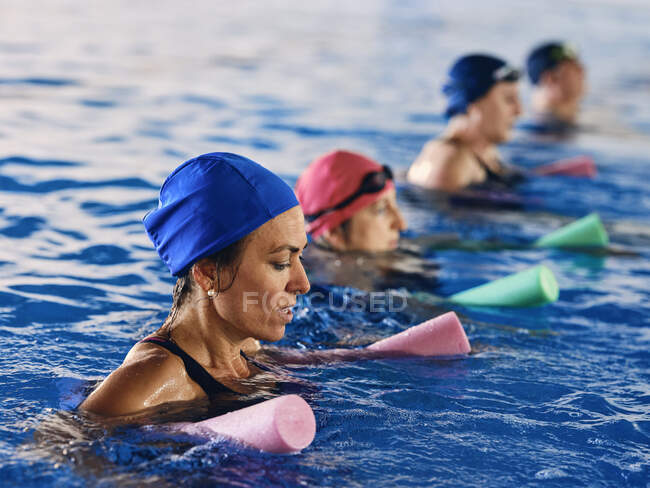 Вид сбоку на группу людей в купальниках, практикующихся с пенной лапшой в бассейне во время водной аэробики — стоковое фото