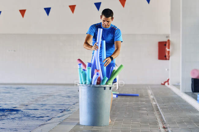 Чоловік, який плаває, кладе локшину з піни у відро після тренування з аеробіки в басейні. — стокове фото