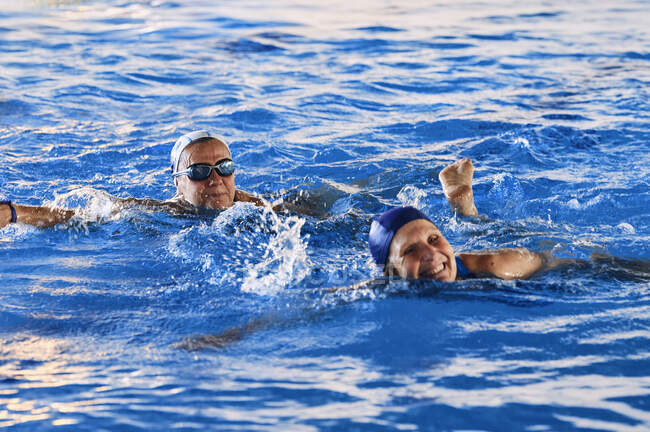 Lächelnde Frauen mittleren Alters in Badebekleidung, die im Pool schwimmen und gemeinsam Wassergymnastik machen — Stockfoto