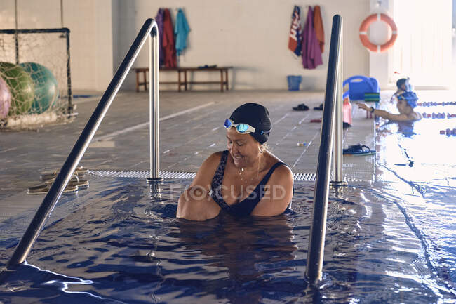 Вміст жінки середнього віку в кепці та купальнику, що готується до плавання в басейні під час водної аеробіки — стокове фото