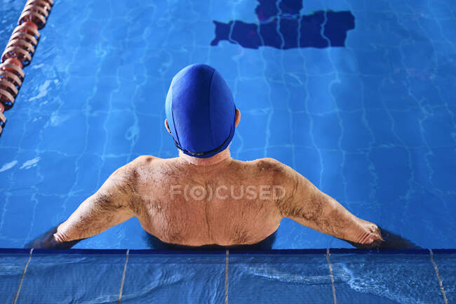 From above back view of anonymous elderly male swimmer in cap standing in water in swimming pool — Stock Photo