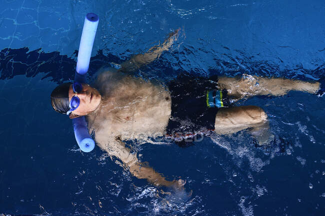 Верхний вид мужчины средних лет в очках, плавающего на спине на пенной лапше во время водной аэробики в бассейне — стоковое фото