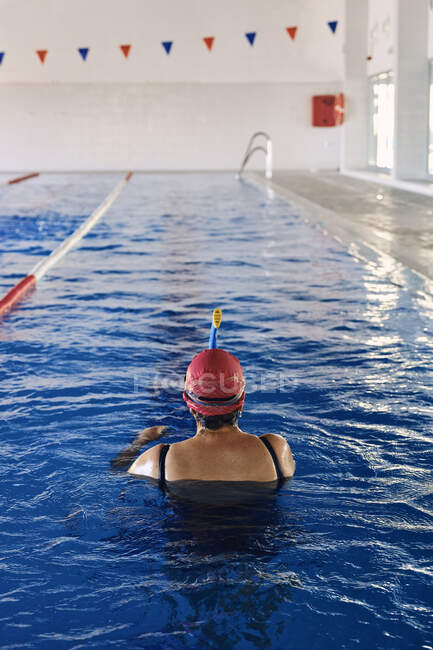 Vue de dessus du dos d'une femme âgée anonyme nageuse en bonnet debout dans l'eau dans la piscine — Photo de stock