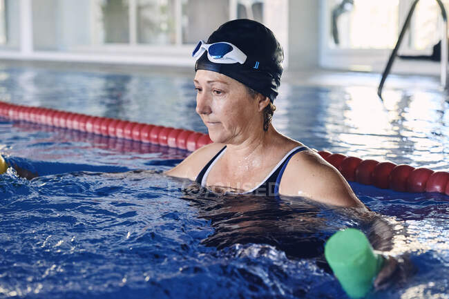 Nageuse mature concentrée faisant de l'exercice avec des haltères dans la piscine pendant l'entraînement d'aérobic aquatique — Photo de stock