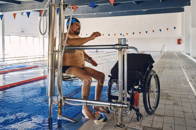 Mature male sitting on chair of swimming pool lift near wheelchair before training — Stock Photo