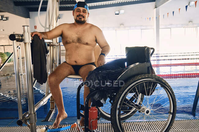 Homme mature assis sur la chaise de la piscine ascenseur près du fauteuil roulant avant l'entraînement — Photo de stock
