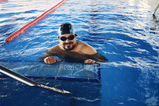 Очарованный мужчина в шапке плавает в бассейне и делает упражнения во время занятий водной аэробикой — стоковое фото
