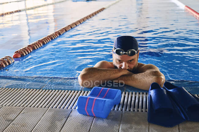 Tired male swimmer leaning on edge of pool and having break during active training — Stock Photo