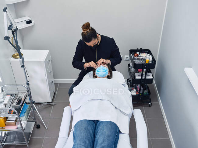 From above of professional cosmetician applying cleanser on eyelashes of female client during beauty treatment in salon — Stock Photo