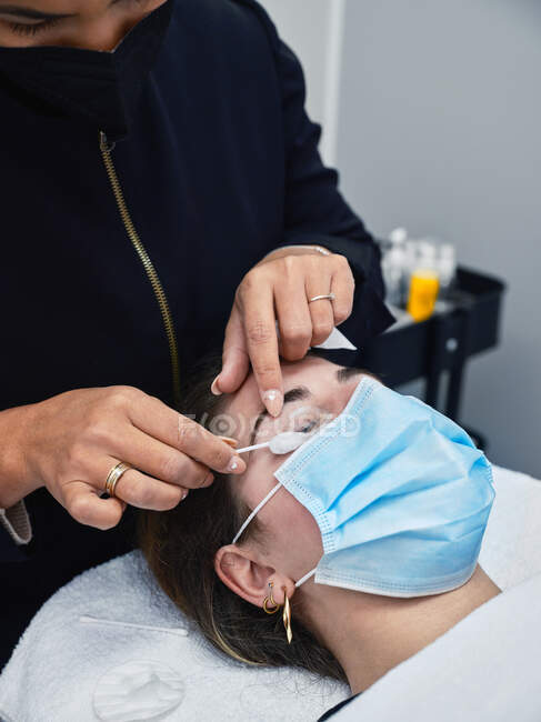 Closeup of crop anonymous cosmetician applying eyelash foam cleanser on female customer during beauty procedure in salon — Stock Photo