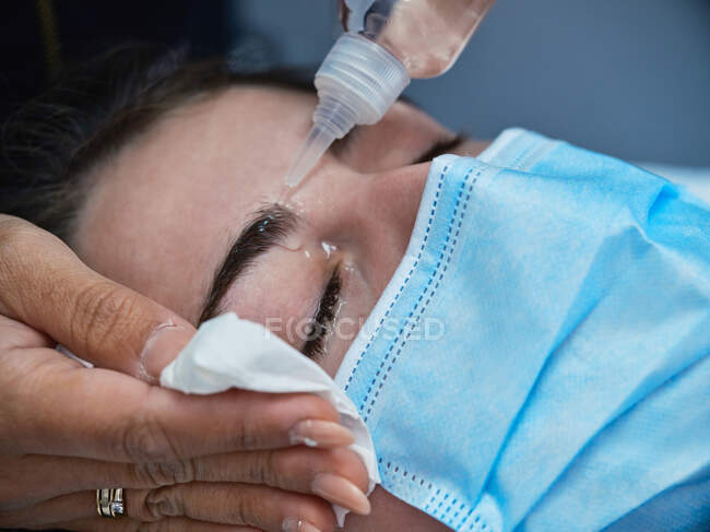 Professionelle Kosmetikerin behandelt Wimpern einer Patientin in Schutzmaske im modernen Schönheitssalon mit Standlampe — Stockfoto