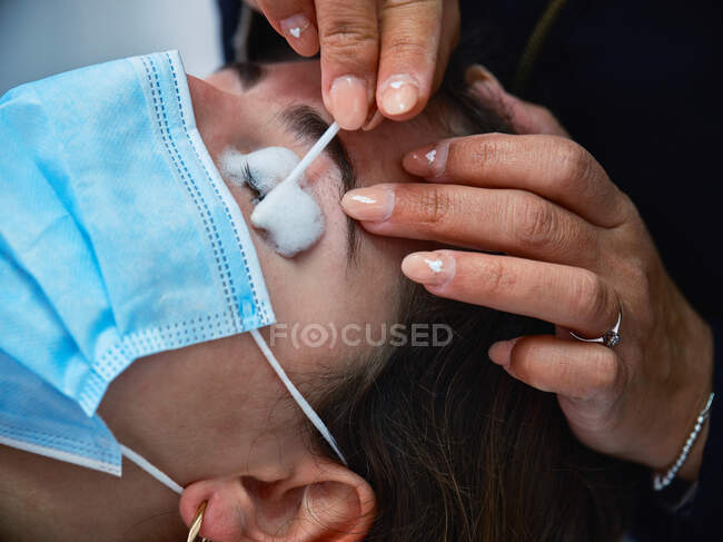 Close-up de cultura anônimo cosmetician aplicando limpador de espuma de pestana no cliente feminino durante o procedimento de beleza no salão — Fotografia de Stock