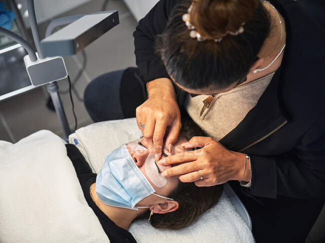 From above crop anonymous beauty master applying lash lift shield on eyelid of female client during eyelash treatment in salon — Stock Photo